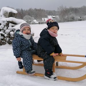 zwei Little Munchkins sitzen auf einem Holzschlitten im Schnee und lächeln