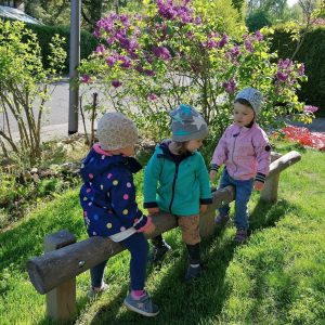 Little Mucnhkins sitzen hintereinadner auf Wackelbalken im eigenen Spielplatz